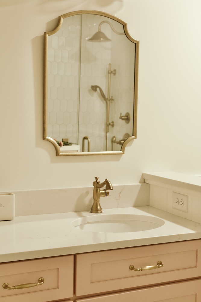 Bathroom vanity with brass faucet and mirror reflecting shower by Trade Works Remodeling in Louisville, KY